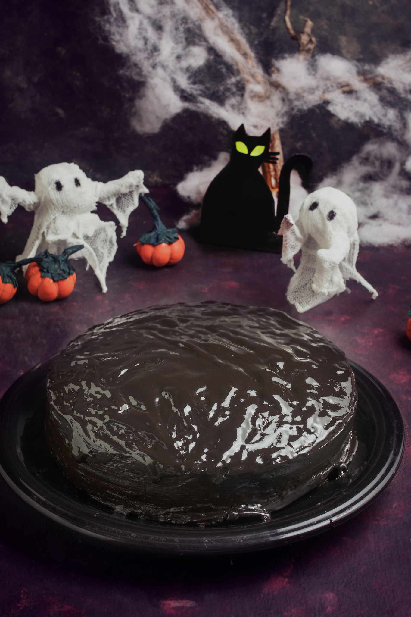 Chocolate Ghoulyard Cake surrounded by ghost, pumpkin and black cat Halloween decorations.